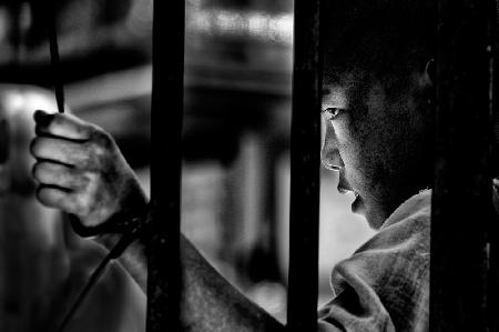 Ein junger Mönch hinter den Gittern einer buddhistischen Schule